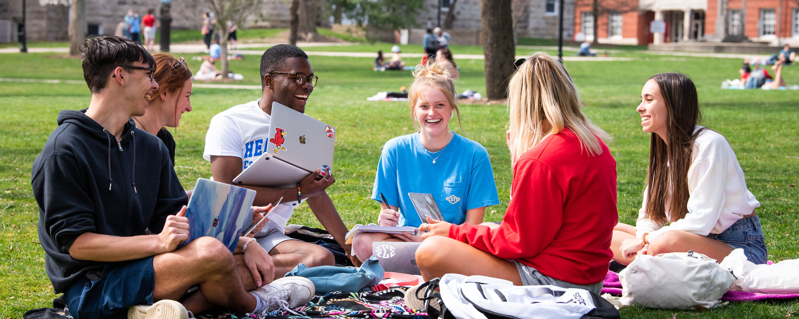 A group of students chat while sitting out on the quad.